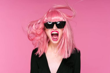 Pembe peruklu ve güneş gözlüklü genç bir kadın stüdyoda poz veriyor. 