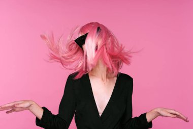 Pembe peruklu ve güneş gözlüklü genç bir kadın stüdyoda poz veriyor. 