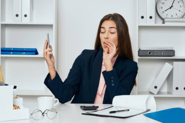 Genç, güzel, yorgun iş kadını ofiste masa başında oturuyor.