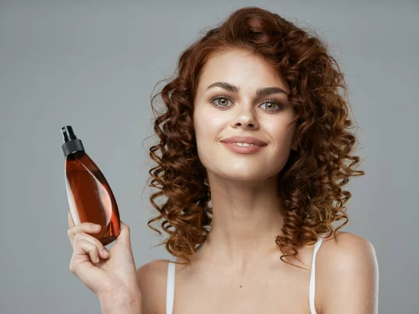 Young beautiful woman with curly hair holding hair spray. Studio shot