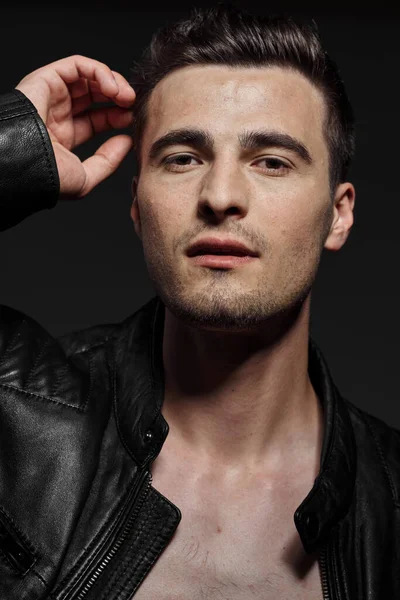 Young handsome man in leather jacket posing in studio on dark background