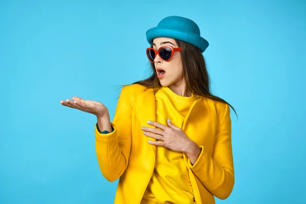 young beautiful woman in yellow jacket  showing something   in Studio with blue Background.
