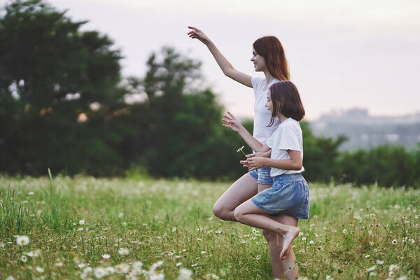 Young mother and her daughter having fun on camomile field