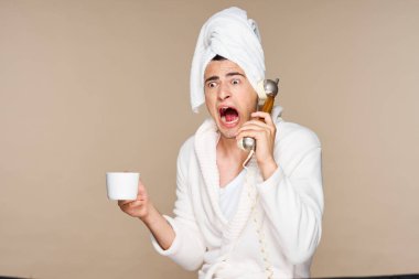 Bornozlu, elinde bir fincan kahveyle telefonda konuşan genç, duygusal bir adam. Stüdyo çekimi. İzole edilmiş