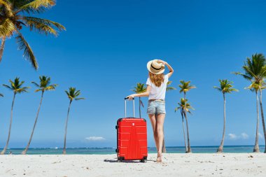  Kumsalda kırmızı valizli genç bir kadın.