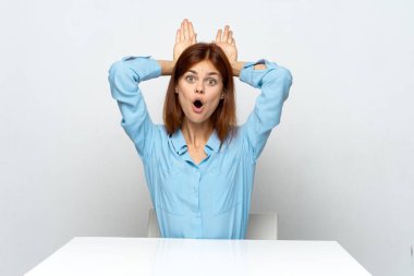 Genç ve güzel bir iş kadını ofiste oturmuş kulaklarını gösteriyor. 