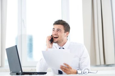 İş konsepti. Ofiste akıllı telefondan konuşan genç bir işadamı. 