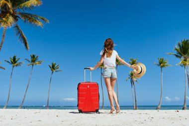  Kumsalda kırmızı valizli genç bir kadın.