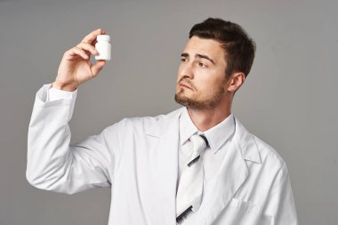 Stüdyo çekimi. Genç doktor gri arka planda izole edilmiş haplara bakıyor. 