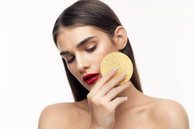 Genç ve güzel bir kadın yüzünü süngerle temizliyor. Güzellik rutini. Stüdyo çekimi