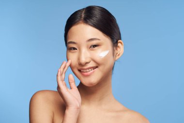 Stüdyoda mavi arka planda genç bir Asyalı kadın var. 