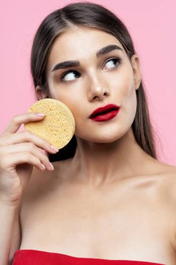 Cilt bakımı ve güzellik. Pembe arka planda süngerle cildini temizleyen güzel bir kadının portresi.