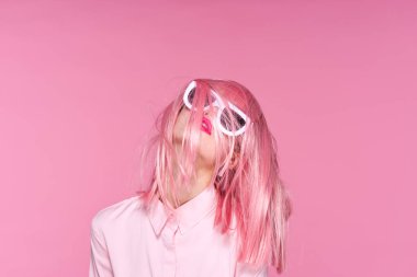 Pembe peruklu ve pembe arka planda güneş gözlüklü genç bir kadın.