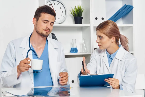 Young doctor with coffee and nurse with clipboard in hospital