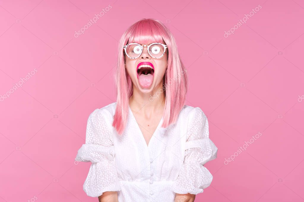 Young woman in pink wig and glasses showing tongue   on pink background