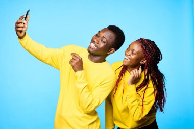 Genç ve güzel bir çift stüdyoda mavi arka planda selfie çekiyor.