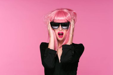 Pembe peruklu ve güneş gözlüklü genç bir kadın stüdyoda poz veriyor. 