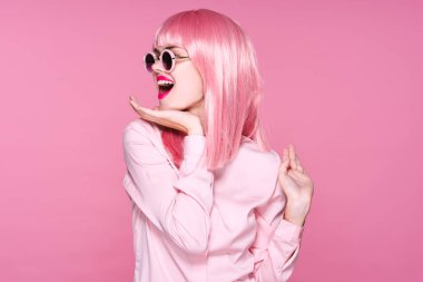 Pembe peruklu ve güneş gözlüklü genç bir kadın stüdyoda poz veriyor. 