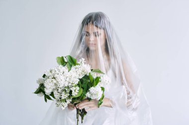 Plastik çarşafın altında elinde çiçekler olan genç bir kadın. Ekoloji kavramı