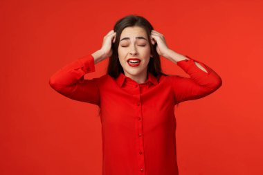 Stüdyo çekimi. Kırmızılı genç ve güzel bir kadın. Kırmızı arka planda izole edilmiş baş ağrısı var.