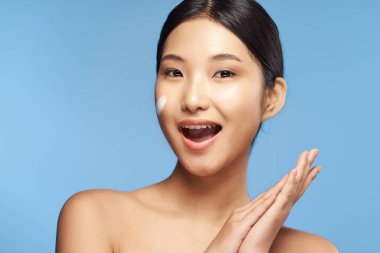 Genç Asyalı kadın yüzüne nemlendirici sürüyor. 