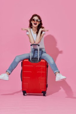 Stüdyoda kırmızı valizli genç bir kadın var.