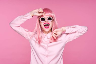 Pembe peruklu ve güneş gözlüklü genç bir kadın stüdyoda poz veriyor. 