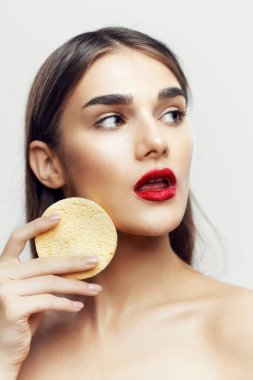 Genç ve güzel bir kadın yüzünü süngerle temizliyor. Güzellik rutini. Stüdyo çekimi