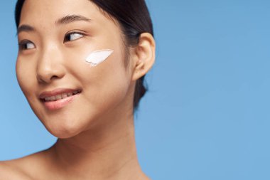 Genç Asyalı kadın yüzüne nemlendirici sürüyor. 