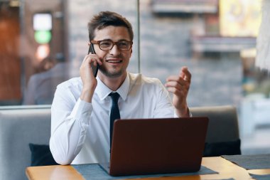 Bilgisayarlı genç işadamı ofiste akıllı telefondan konuşuyor. 