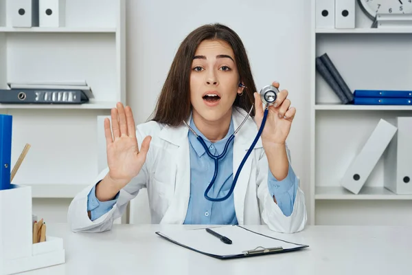 Young confused woman doctor with stethoscope sitting at desk