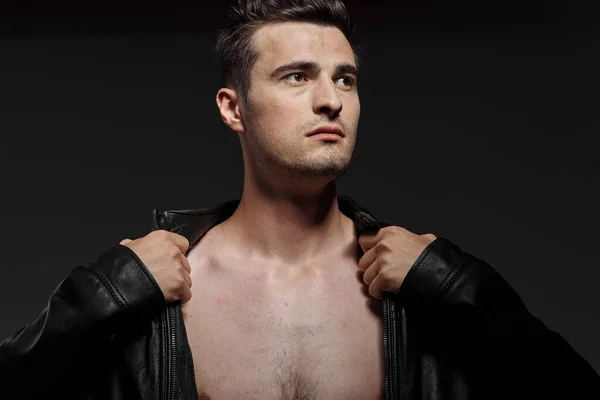 Young handsome man in leather jacket posing in studio on dark background