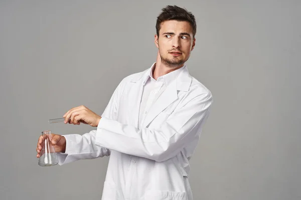 confused Doctor in lab coat with test tubes on grey background. Studio shot