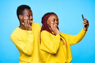 Genç ve güzel bir çift stüdyoda mavi arka planda selfie çekiyor.