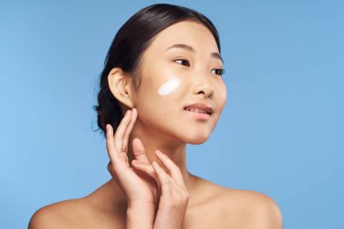 Genç Asyalı bir kadın mavi arka plandan stüdyoya bakıyor. 