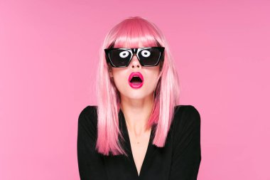 Pembe peruklu ve güneş gözlüklü genç bir kadın stüdyoda poz veriyor. 
