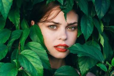 Yüzünde yapraklarla poz veren genç ve güzel bir kadın.