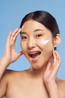 Genç Asyalı kadın yüzüne nemlendirici sürüyor. 