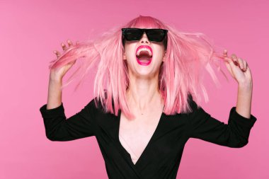 Pembe peruklu ve güneş gözlüklü genç bir kadın stüdyoda poz veriyor. 