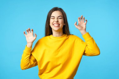 Stüdyoda elleri havada genç bir kadın mavi arka planda izole edilmiş. 