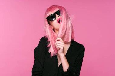 Pembe peruklu ve güneş gözlüklü genç bir kadın stüdyoda poz veriyor. 