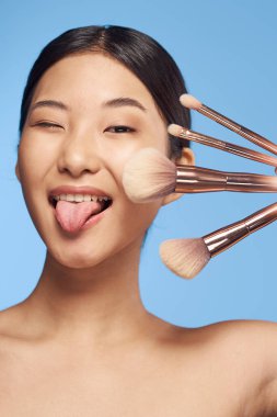 young asian woman  holding brushes sticking out tongue 