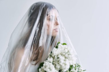 Plastik çarşafın altında elinde çiçekler olan genç bir kadın. Ekoloji kavramı