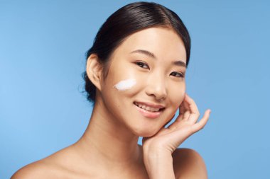 Genç Asyalı kadın yüzüne nemlendirici sürüyor. 