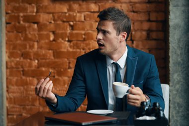 Elinde kahve fincanı olan kızgın bir iş adamı.