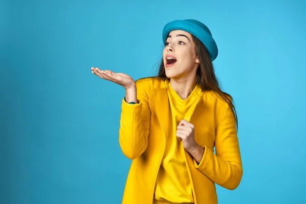 young beautiful woman in yellow jacket   showing something  in Studio with blue Background.