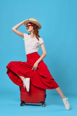 Stüdyoda kırmızı valizli genç bir kadın var.