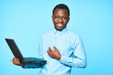 Genç Afrikalı iş adamı dizüstü bilgisayarını mavi arka planda tutuyor.