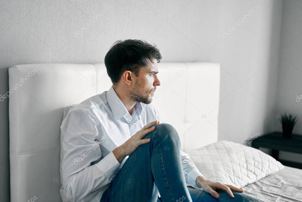 sad man sitting in bed indoors and looking aside loneliness