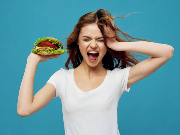 Энергичная женщина с открытым ртом держит гамбургер — стоковое фото